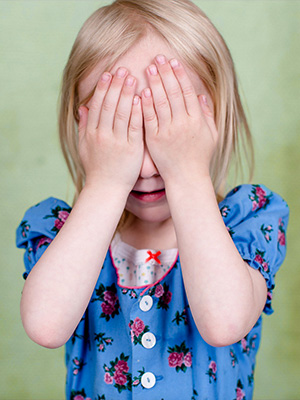 Une petite fille qui se couvre le visage et les yeux avec ses mains.